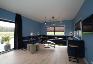 Sala del Amalia Familia lodge en Hofparken Wiltershaar, Países Bajos, con paredes azules, sofás y grandes ventanales.