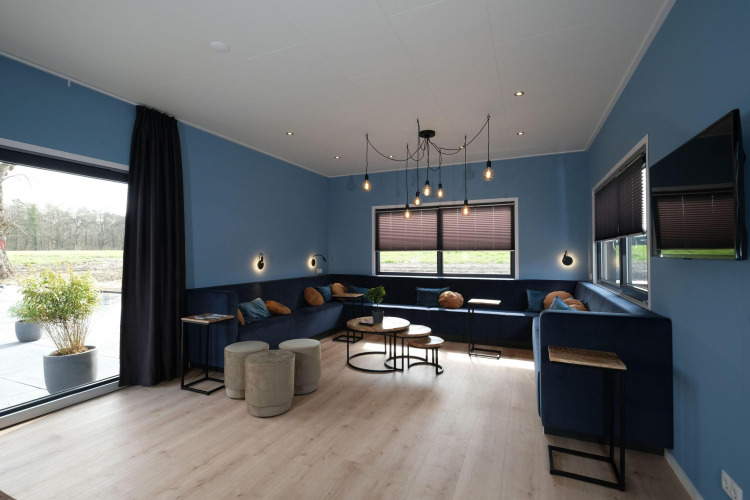 Sala del Amalia Familia lodge en Hofparken Wiltershaar, Países Bajos, con paredes azules, sofás y grandes ventanales.