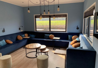 Moderne loungehoek in Amalia Familia lodge, Hofparken Wiltershaar, Nederland, met blauwe zetels en muren.