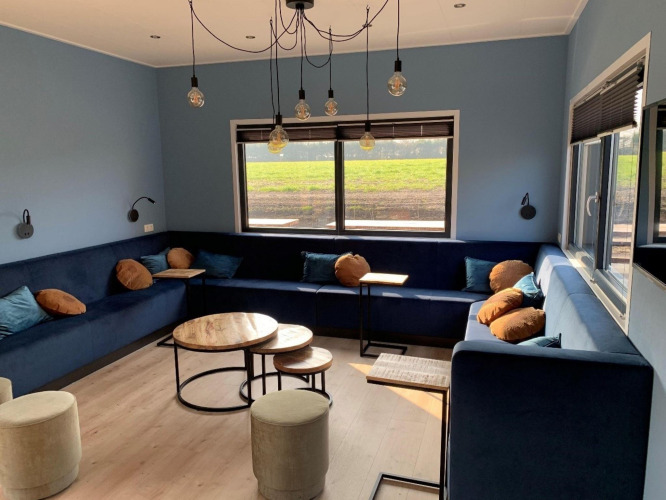 Modernes Loungezimmer in der Amalia Familia Lodge, Hofparken Wiltershaar, mit blauen Wänden und Sofas.