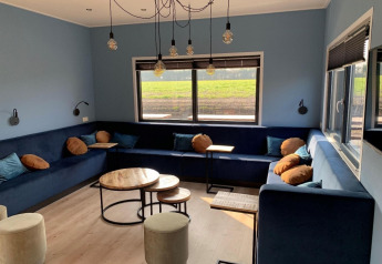 Moderne loungehoek in Amalia Familia lodge, Hofparken Wiltershaar, Nederland, met blauwe zetels en muren.
