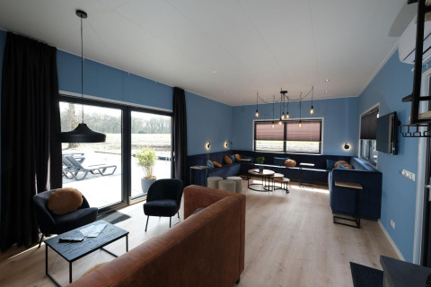 Stue med blå vægge, store vinduer, moderne møbler og udsigt til terrasse ved Amalia Familia, Hofparken Wiltershaar.