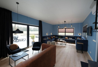 Stue med blå vægge, store vinduer, moderne møbler og udsigt til terrasse ved Amalia Familia, Hofparken Wiltershaar.