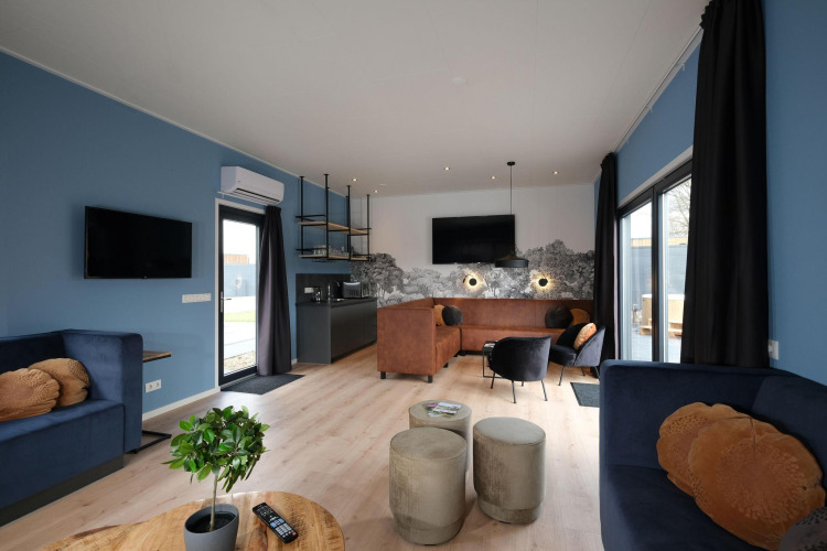 Modernes Wohnzimmer in der Amalia Familia Lodge im Hofparken Wiltershaar, Niederlande, mit blauen Wänden und stilvollen Möbeln.