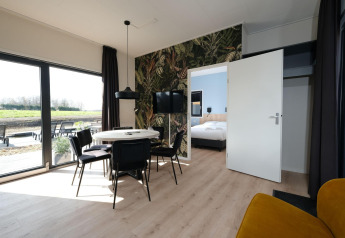 Modern lodge-interieur met eetplaats, zwarte stoelen en zicht op slaapkamer in Hofparken Wiltershaar.