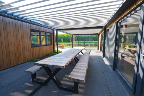 Udendørs spiseområde med træbord og bænke under pergola ved Amalia Familia i Hofparken Wiltershaar, Holland.