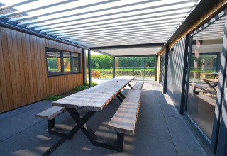 Udendørs spiseområde med træbord og bænke under pergola ved Amalia Familia i Hofparken Wiltershaar, Holland.