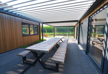 Overdekte buiteneettafel met houten banken bij Amalia Familia, Hofparken Wiltershaar, Nederland.