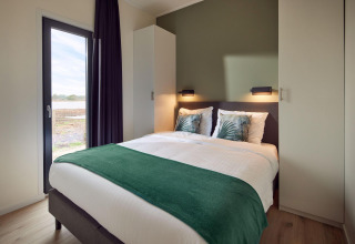 Dormitorio moderno con cama doble, detalles verdes y vista exterior en Holiday villa Amalia 6, Países Bajos.