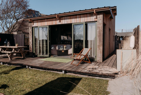 Foto van de Juttershut-lodge bij Duynpark Het Zwanenwater in Nederland met terras en buitenmeubilair.