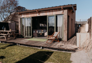 Foto van de Juttershut-lodge bij Duynpark Het Zwanenwater in Nederland met terras en buitenmeubilair.