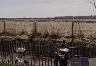 Een fiets staat bij een hek aan een veld bij Juttershut Lodge, Duynpark Het Zwanenwater, Nederland.