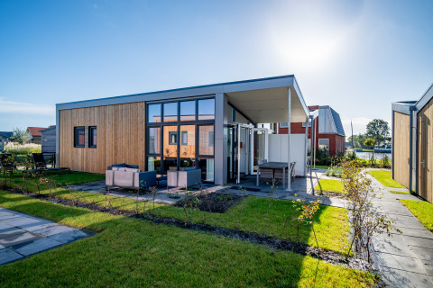 Modern tiny house with wooden cladding, large windows, and outdoor seating at Tusken de Marren, Netherlands.