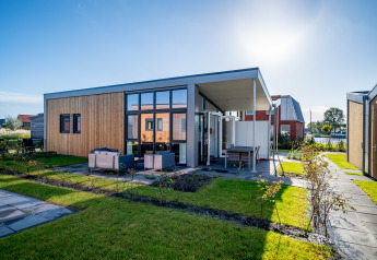 Modern tiny house with wooden cladding, large windows, and outdoor seating at Tusken de Marren, Netherlands.