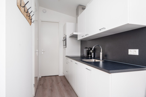 Moderne lille lyst køkken med hvide skabe og sorte bordplader i et tiny house ved Tusken de Marren.