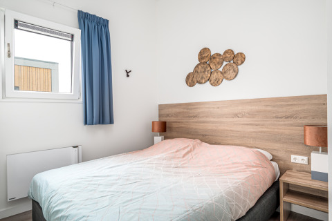 Slaapkamer in Knilles Luxe tiny house bij Tusken de Marren, Nederland, met bed en houten wanddecoratie.