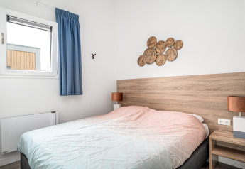 Bedroom inside Knilles Luxe tiny house at Tusken de Marren, Netherlands, with double bed and wall art.