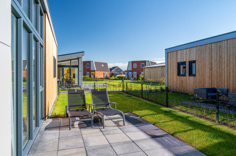 Solrig terrasse med liggestole ved Knilles Luxe tiny house i Tusken de Marren, Holland, omgivet af grønne haver.