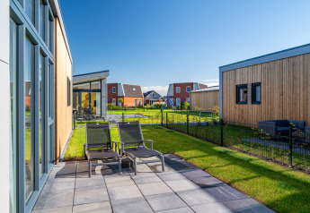Solrig terrasse med liggestole ved Knilles Luxe tiny house i Tusken de Marren, Holland, omgivet af grønne haver.