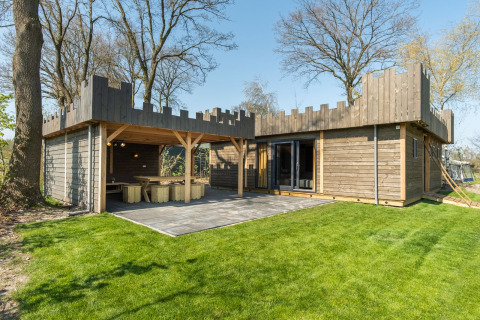 Modern wooden lodge with castle design, patio and green lawn at Kampeerdorp de Zandstuve, the Netherlands.