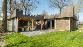 Modern wooden lodge with castle design, patio and green lawn at Kampeerdorp de Zandstuve, the Netherlands.