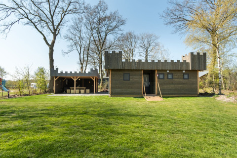 En træhytte formet som et slot med tårne og en åben pavillon ved Kampeerdorp de Zandstuve, Nederlandene.