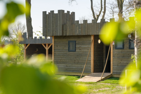 Trælodge med slots-design i Castle Uylenburght, Kampeerdorp de Zandstuve, Nederlandene, set gennem blade.