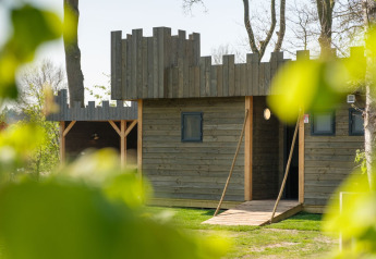 Cabaña de madera con diseño de castillo en Castle Uylenburght, Kampeerdorp de Zandstuve, Países Bajos, vista entre hojas.