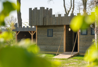 Houten kasteel-lodge bij Castle Uylenburght, Kampeerdorp de Zandstuve, Nederland, gezien tussen bladeren.