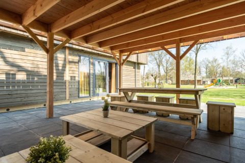Covered terrace with wooden tables and benches at Castle Uylenburght lodge in Kampeerdorp de Zandstuve, Netherlands.