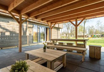 Covered terrace with wooden tables and benches at Castle Uylenburght lodge in Kampeerdorp de Zandstuve, Netherlands.