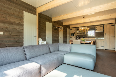 Moderne lodge stue i Castle Uylenburght, Kampeerdorp de Zandstuve, med sofa og åbent køkken.