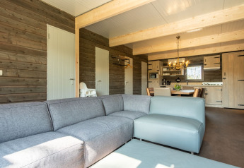 Sala luminosa de lodge en Castle Uylenburght, Kampeerdorp de Zandstuve, con sofá y cocina abierta.