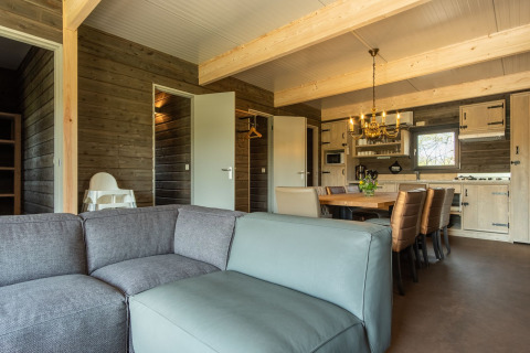 Zona de estar con sofá, mesa de comedor y cocina en una cabaña de madera en Castle Uylenburght, Kampeerdorp de Zandstuve, Países Bajos.