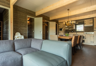 Salon avec canapé, table à manger et cuisine dans un chalet en bois à Castle Uylenburght, Kampeerdorp de Zandstuve, Pays-Bas.