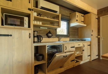 Cucina in legno chiaro con mensole aperte, lavastoviglie, microonde e macchina da caffè in un lodge a Kampeerdorp de Zandstuve.