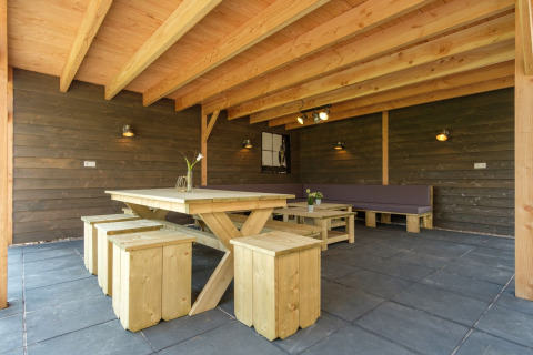 Zona de estar exterior cubierta con mesa y bancos de madera en Castle Uylenburght, Kampeerdorp de Zandstuve.