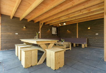 Zona de estar exterior cubierta con mesa y bancos de madera en Castle Uylenburght, Kampeerdorp de Zandstuve.