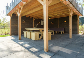 Zona pranzo all'aperto coperta con tavolo e panche in legno presso Castle Uylenburght, Kampeerdorp de Zandstuve.