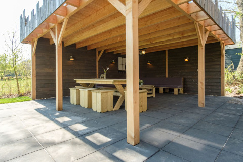 Overdekte buitenruimte met houten tafel en banken aan Castle Uylenburght, Kampeerdorp de Zandstuve.