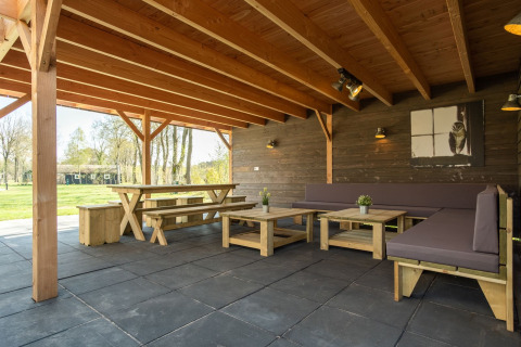 Overdekt buitenterras met houten banken en tafels bij Castle Uylenburght, Kampeerdorp de Zandstuve, Nederland.