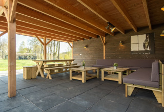 Overdekte buitenruimte met houten banken en tafels bij Castle Uylenburght, Kampeerdorp de Zandstuve.