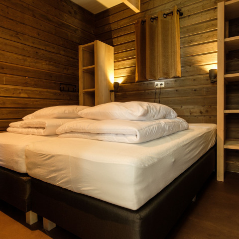 Gezellige slaapkamer met twee bedden, houten wanden en warme verlichting in Castle Uylenburght, Kampeerdorp de Zandstuve.