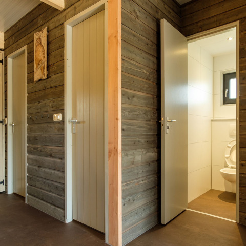 Baños modernos con paneles de madera gris y puertas abiertas en Castle Uylenburght, Kampeerdorp de Zandstuve.