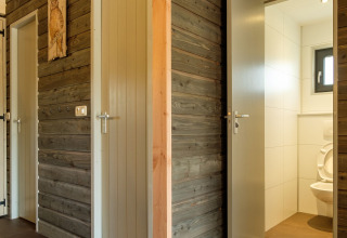 Modern restrooms with gray wooden paneling and open doors at Castle Uylenburght, Kampeerdorp de Zandstuve.