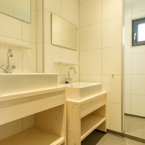 Salle de bains moderne avec deux lavabos blancs, meubles en bois clair et miroirs dans une auberge.