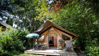 Tenda safari chiamata Staircase tent immersa nella natura, con veranda in legno e arredi da esterno.
