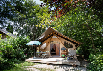 Safari tent ‘Staircase tent’ in een groene omgeving, met houten terras en comfortabele buitenstoelen.