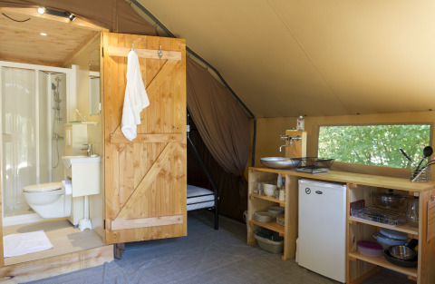 Inside view of a glamping tent with wooden bathroom, small kitchen, fridge, and window to nature.