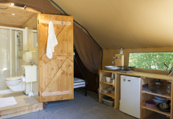 Intérieur d'une tente glamping avec salle de bain en bois, kitchenette, réfrigérateur et fenêtre.